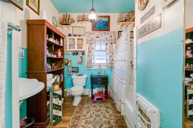 bathroom with hardwood / wood-style floors, heating unit, toilet, and shower / tub combo with curtain