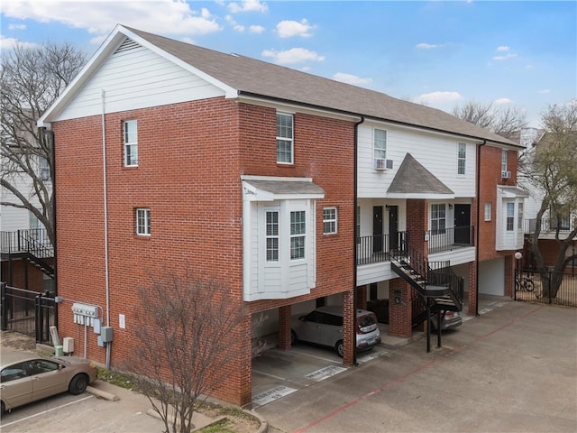 back of house with stairway, uncovered parking, brick siding, and a shingled roof