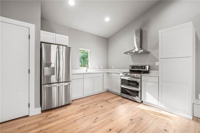 kitchen featuring appliances with stainless steel finishes, light wood-type flooring, wall chimney range hood, sink, and white cabinetry