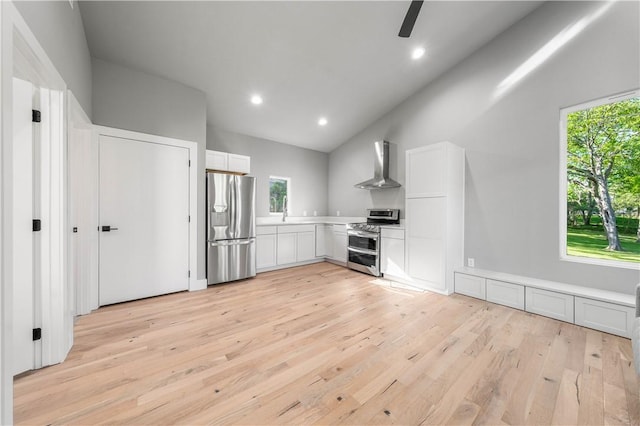 kitchen featuring appliances with stainless steel finishes, light wood-type flooring, wall chimney exhaust hood, white cabinets, and lofted ceiling