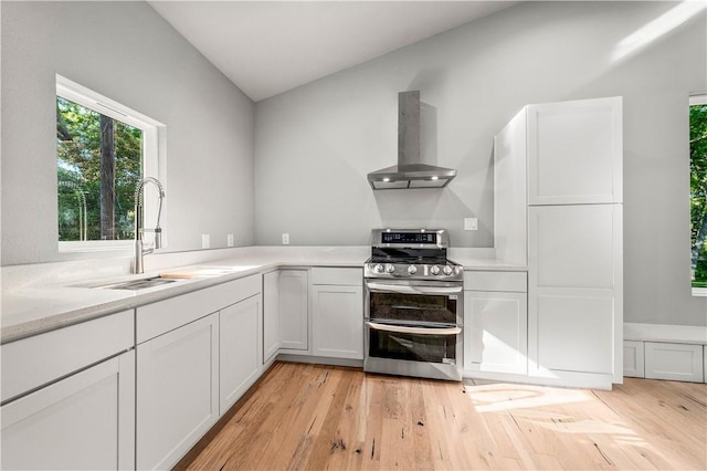 kitchen with wall chimney exhaust hood, white cabinetry, stainless steel range, and light hardwood / wood-style flooring