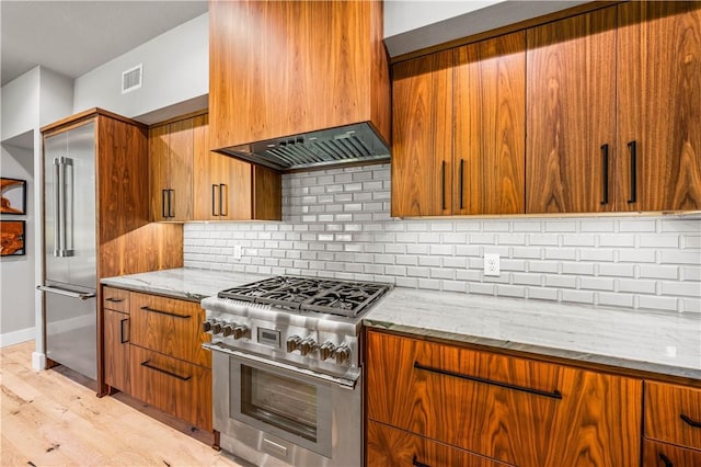 kitchen with custom exhaust hood, high quality appliances, backsplash, light wood-type flooring, and light stone counters