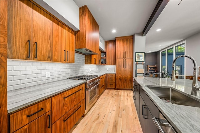 kitchen featuring high end range, sink, decorative backsplash, light hardwood / wood-style floors, and light stone counters