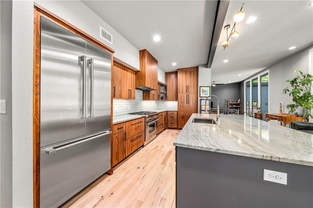 kitchen with light wood-type flooring, ceiling fan, sink, a large island with sink, and high quality appliances