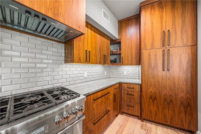 kitchen featuring backsplash, light stone counters, custom range hood, high end stainless steel range oven, and light hardwood / wood-style flooring