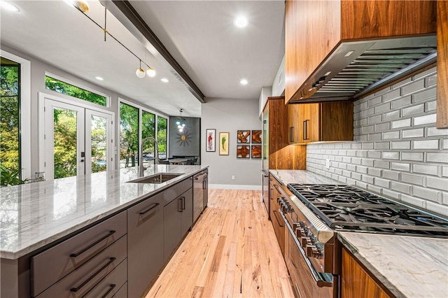 kitchen with light stone countertops, wall chimney exhaust hood, stainless steel appliances, sink, and light hardwood / wood-style flooring