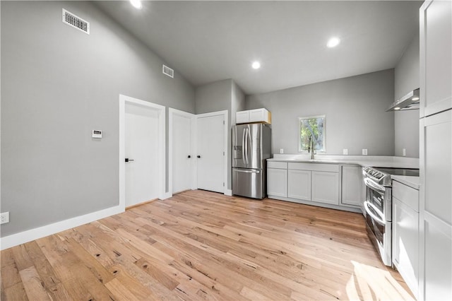 kitchen featuring appliances with stainless steel finishes, light wood-type flooring, wall chimney exhaust hood, sink, and white cabinetry