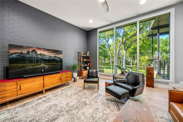 sitting room with light hardwood / wood-style flooring, ceiling fan, and brick wall