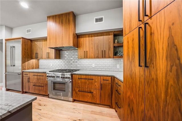 kitchen featuring decorative backsplash, light wood-type flooring, light stone counters, and high end appliances