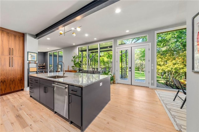 kitchen with light stone counters, sink, light wood-type flooring, and an island with sink