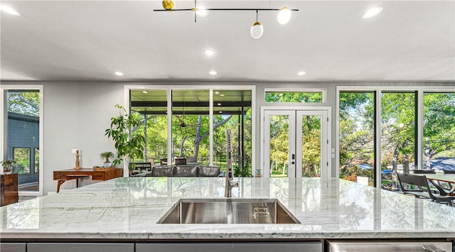 kitchen with light stone counters, a kitchen island with sink, and french doors