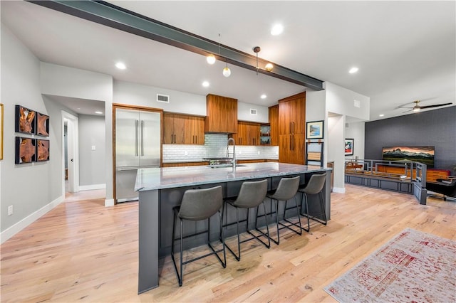 kitchen with light stone countertops, a kitchen breakfast bar, ceiling fan, sink, and light hardwood / wood-style flooring