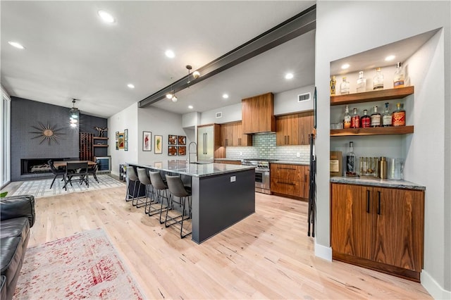 kitchen featuring a breakfast bar, a large island with sink, sink, stainless steel gas range, and light hardwood / wood-style flooring