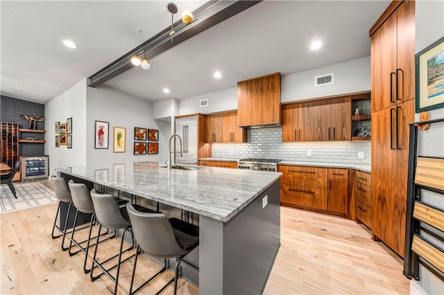 kitchen featuring a large island with sink, a kitchen breakfast bar, sink, light hardwood / wood-style flooring, and custom range hood