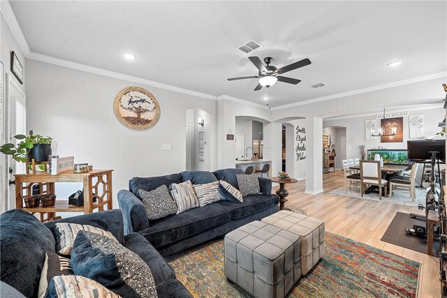 living room featuring ceiling fan with notable chandelier, ornamental molding, and light hardwood / wood-style flooring