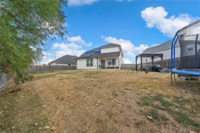 back of property featuring solar panels, a yard, and a trampoline