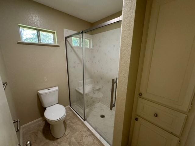 bathroom featuring a shower with door, toilet, and a wealth of natural light