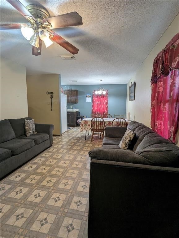 living room featuring visible vents, a textured ceiling, light floors, and ceiling fan with notable chandelier