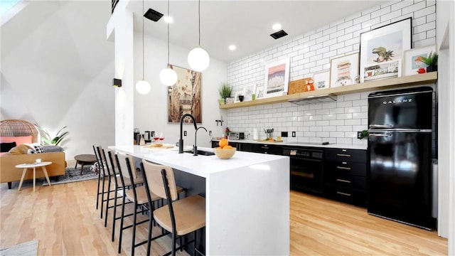 kitchen with a breakfast bar, tasteful backsplash, light hardwood / wood-style floors, black appliances, and decorative light fixtures