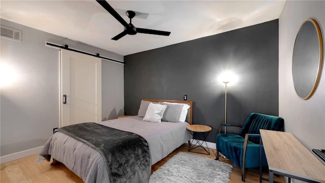 bedroom featuring ceiling fan, a barn door, and light wood-type flooring