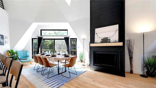 dining space featuring a fireplace, high vaulted ceiling, and light wood-type flooring