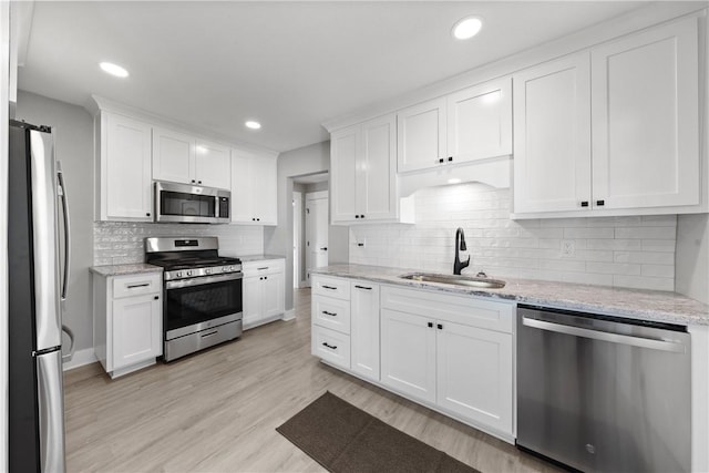 kitchen with appliances with stainless steel finishes, sink, a barn door, light hardwood / wood-style flooring, and white cabinetry