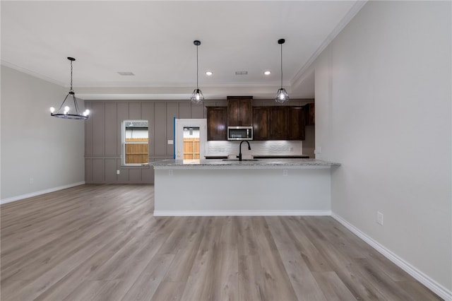 kitchen featuring light stone countertops, dark brown cabinets, kitchen peninsula, and crown molding