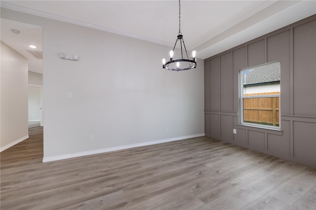 empty room with a notable chandelier, crown molding, and light hardwood / wood-style flooring