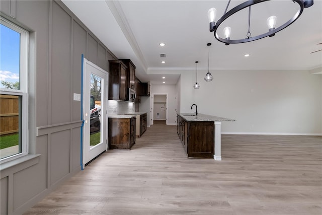 kitchen featuring hanging light fixtures, crown molding, sink, light wood-type flooring, and dark brown cabinetry