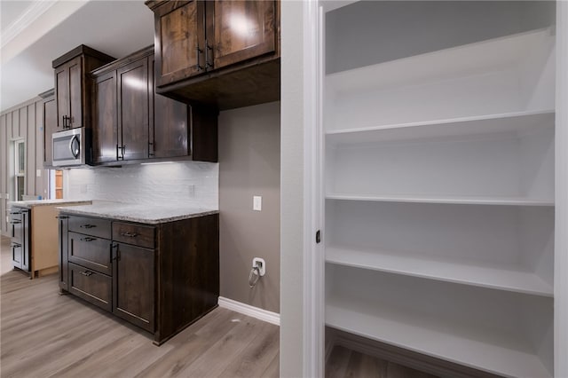 kitchen with dark brown cabinets, light stone countertops, decorative backsplash, and light hardwood / wood-style flooring