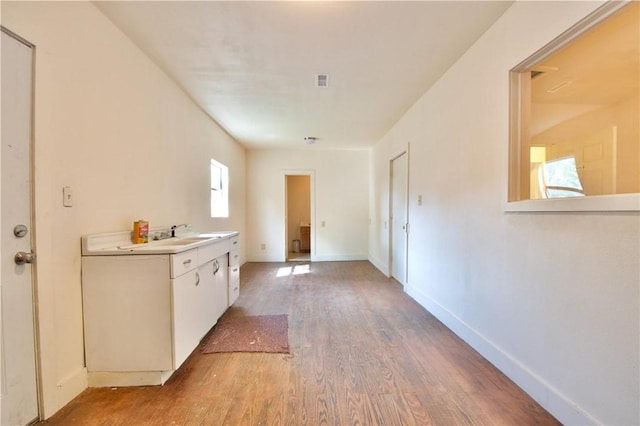 kitchen with wood-type flooring, white cabinetry, and sink