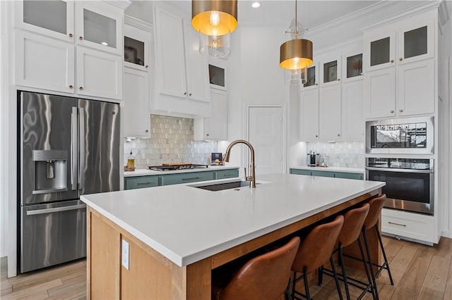 kitchen with sink, an island with sink, light hardwood / wood-style floors, white cabinets, and appliances with stainless steel finishes