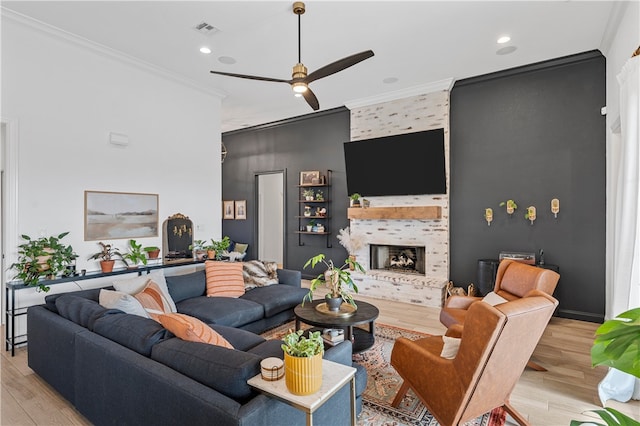 living room with a tile fireplace, crown molding, ceiling fan, and light wood-type flooring