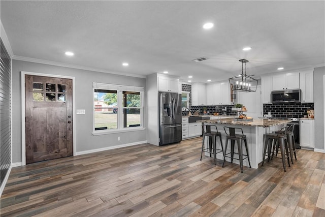 kitchen with white cabinetry, hanging light fixtures, stainless steel appliances, and hardwood / wood-style flooring