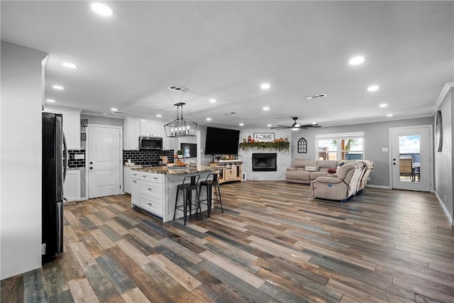 kitchen featuring black refrigerator, hanging light fixtures, a kitchen island, a kitchen bar, and white cabinetry