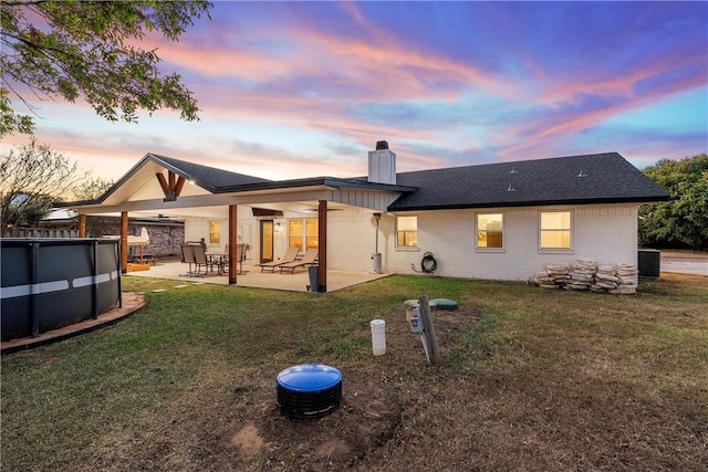 back house at dusk with ceiling fan, a yard, and a patio