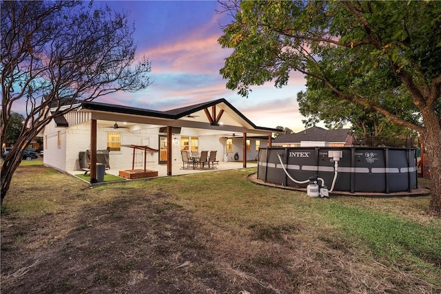 back house at dusk with a patio, ceiling fan, and a lawn