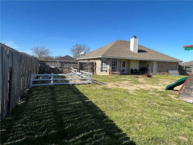 back of house featuring a fenced backyard, a chimney, a yard, a playground, and brick siding