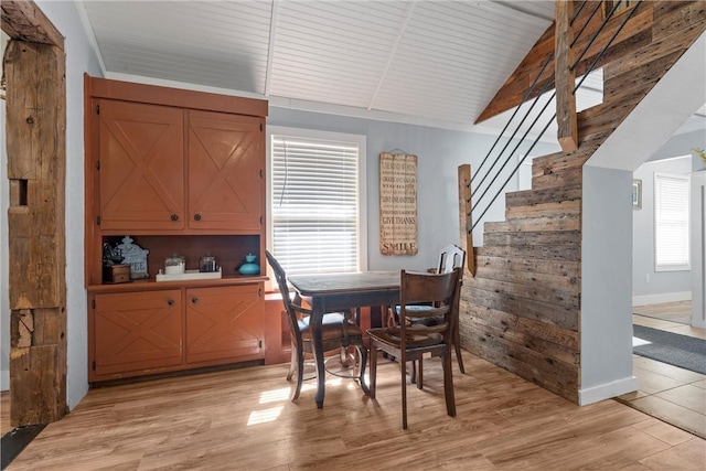 dining space with light wood-style floors, vaulted ceiling with beams, stairway, and wooden walls