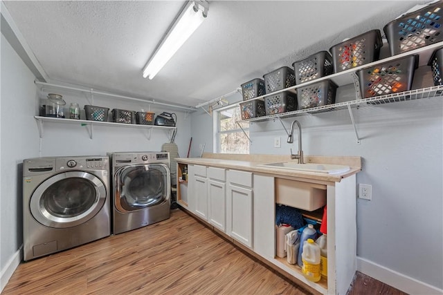 clothes washing area featuring cabinet space, a textured ceiling, light wood-style floors, washing machine and dryer, and a sink