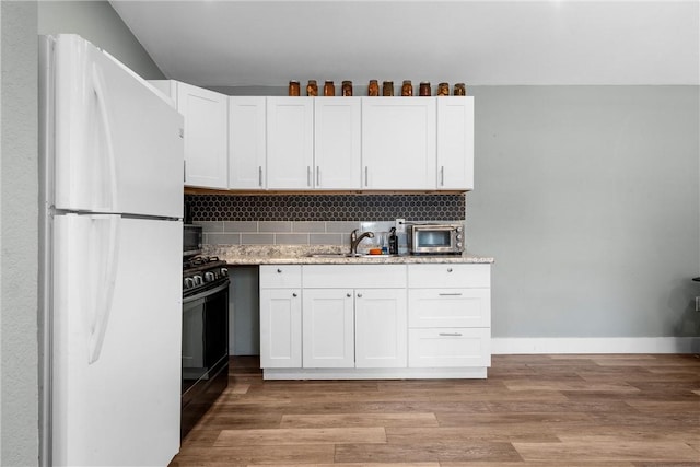 kitchen with black gas range, light wood finished floors, tasteful backsplash, freestanding refrigerator, and a sink