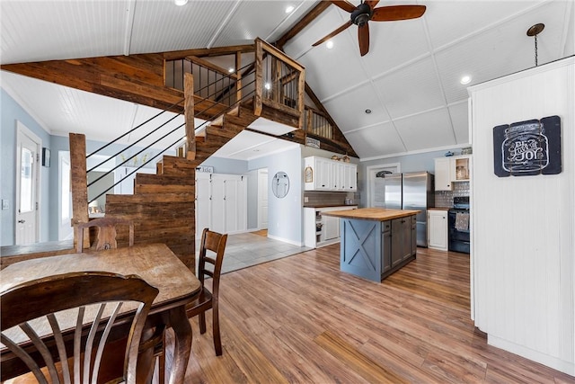 dining area with light wood-style floors, a ceiling fan, high vaulted ceiling, and stairs