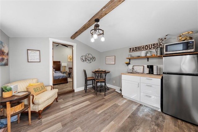 kitchen featuring lofted ceiling with beams, white cabinetry, baseboards, appliances with stainless steel finishes, and light wood-type flooring