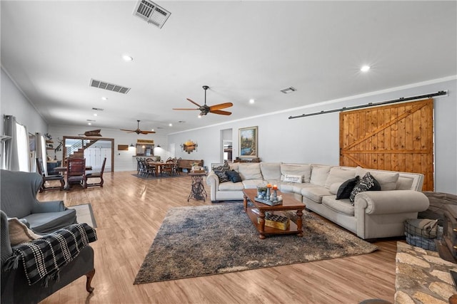 living room with light wood finished floors, a barn door, visible vents, and crown molding