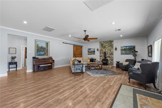 living area featuring light wood finished floors, a barn door, visible vents, a wood stove, and crown molding