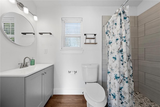 full bath featuring baseboards, toilet, wood finished floors, a tile shower, and vanity