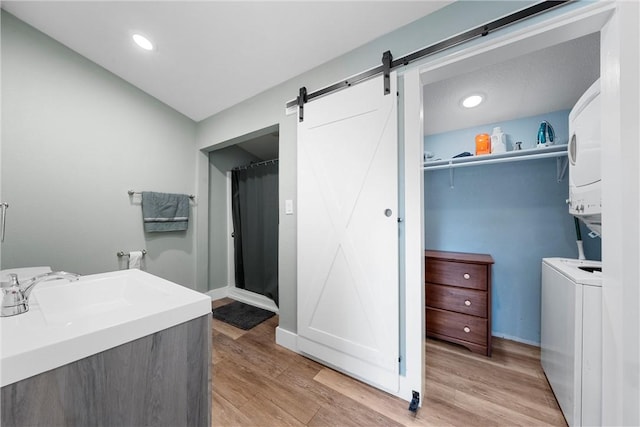 bathroom featuring recessed lighting, stacked washer and clothes dryer, a sink, and wood finished floors