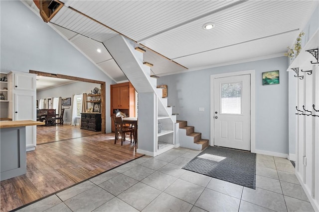 foyer entrance with light tile patterned floors, stairway, vaulted ceiling, and baseboards