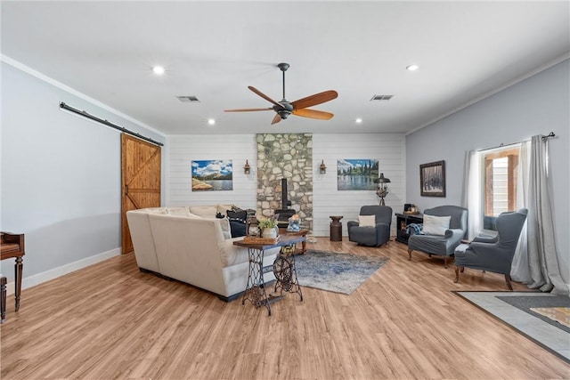 living area featuring a wood stove, light wood-style floors, a barn door, and visible vents