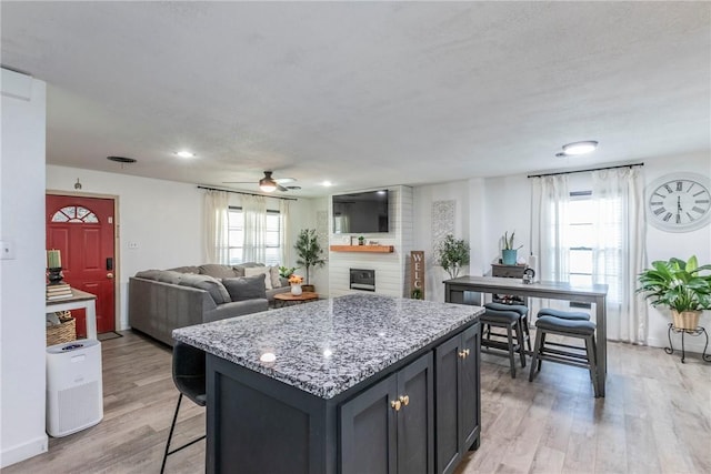 kitchen featuring light stone countertops, light hardwood / wood-style flooring, a kitchen island, and ceiling fan